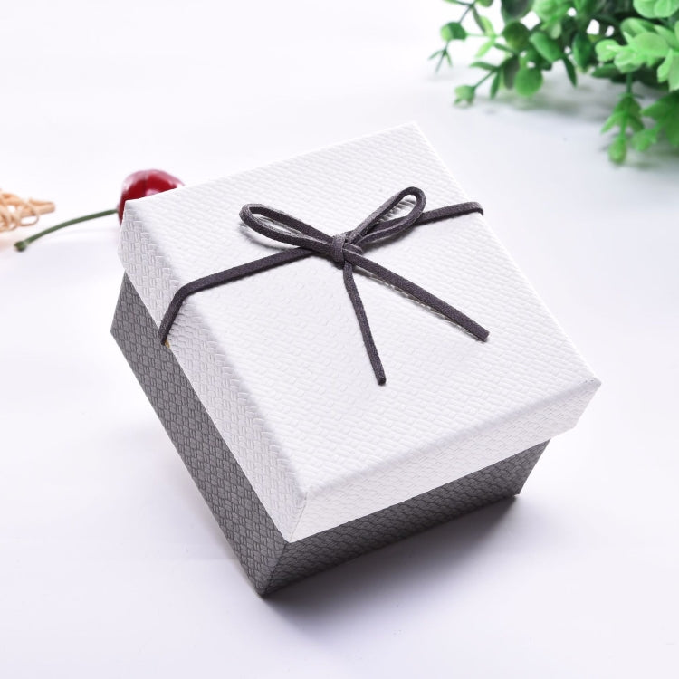 Small jewelry gift box with white lid, gray sides, and black ribbon bow on top.