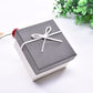 Small jewelry gift box with gray lid, light base, and white ribbon bow on top.