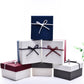 Stacked small jewelry gift boxes with ribbon bows in blue, white, burgundy, and black.