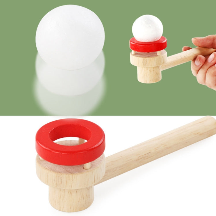 Wooden ball blower puzzle piece with red-ring stopper and white ball; hand holding handle