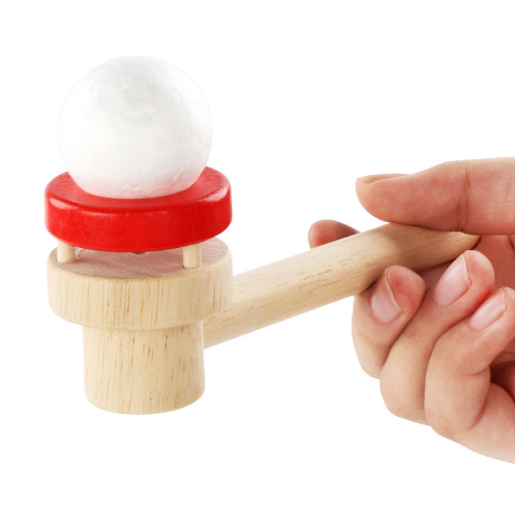 Wooden ball blower with white foam ball on red circular base; hand holding the handle