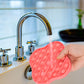 Coral-red silicone pop-it pressing board being pressed near a sink