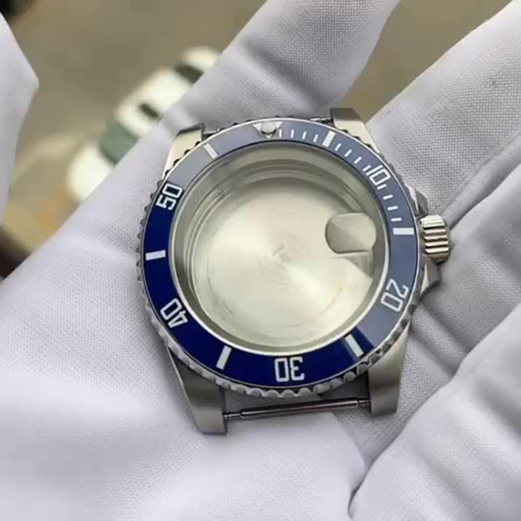Stainless steel watch case with blue bezel and crown, shown on white cloth