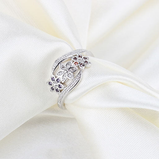 Silver-tone flower diamond ring on white fabric, with purple and clear stones