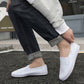 White low-top canvas slip-on sneakers worn with dark jeans and gray cuffs