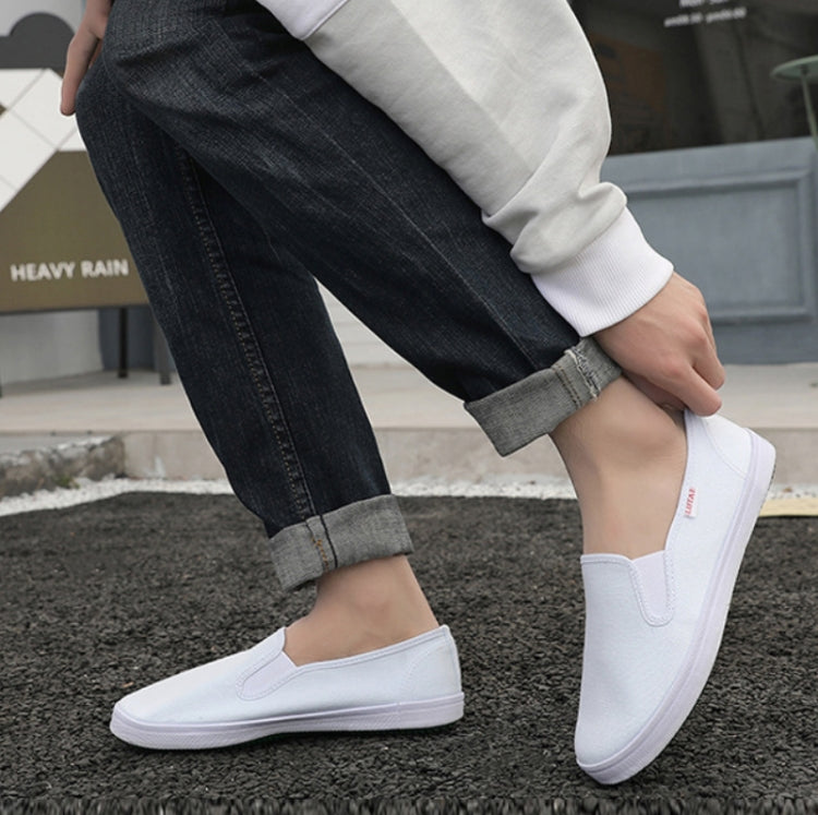 White low-top canvas slip-on sneakers worn with dark jeans and gray cuffs