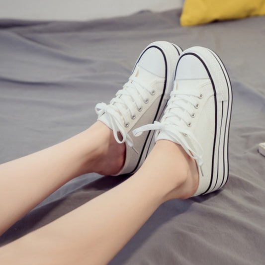 White canvas lace-up platform sneakers with thick sole, worn with rolled cuffs.