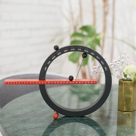 Black circular calendar ornament with month arc, red bar and colorful pegs.
