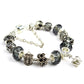 Crystal charm bracelet with dark beads, silver-tone crown-like centerpiece, and filigree spacers