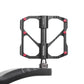 Close-up of black carbon fiber bicycle platform pedal with axles and red screws.