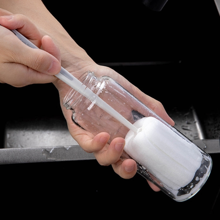 Long-handled sponge brush used to scrub a clear baby bottle in sink