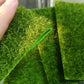 Hand-held green artificial turf sheet with dense faux grass fibers and corner fold