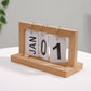 Wooden flipping desk calendar with light wood frame, metal rings, cards showing JAN 01