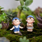 Mini cartoon house figurines on moss: boy in blue and girl in blue at a scene