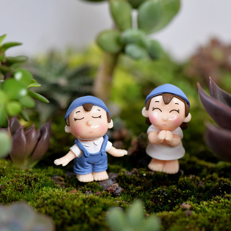 Mini cartoon house figurines on moss: boy in blue and girl in blue at a scene