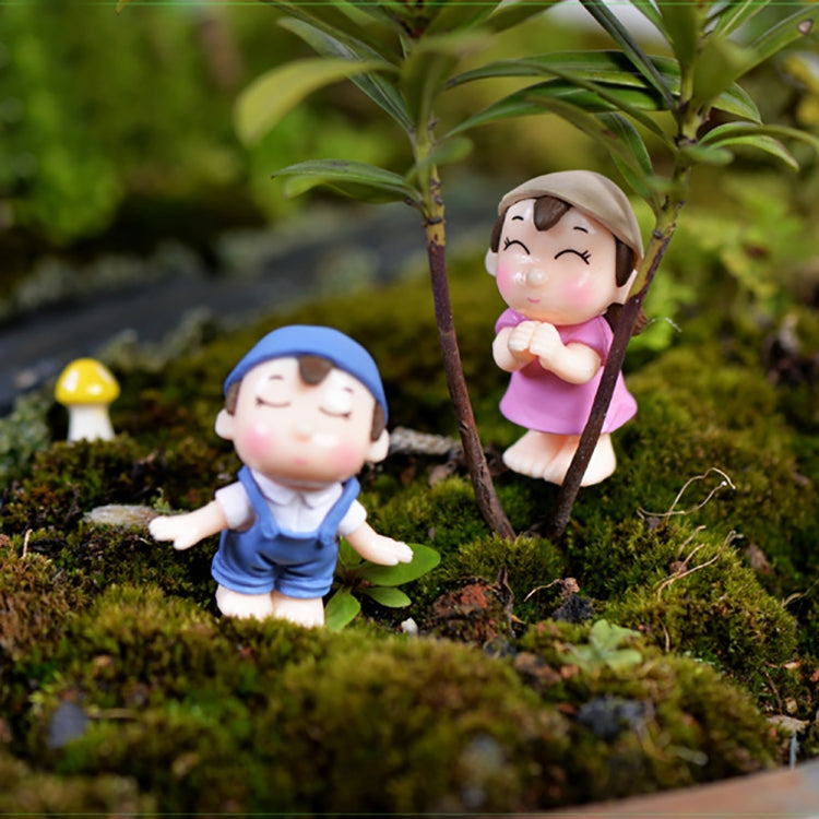 Mini cartoon house figurines on moss with small shrub: girl in pink and boy in blue