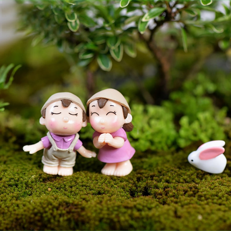 Mini cartoon house figurines on moss: girl in purple, girl in pink, small bunny figure