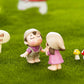 Mini cartoon figurines on grass: girl in pink and boy in purple with small mushrooms