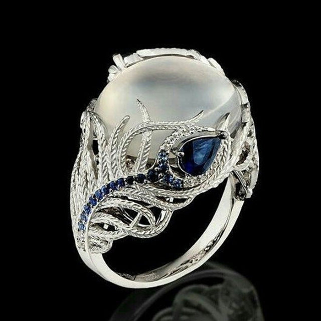Silver-tone ring with oval white stone, blue center gem, and feather pattern band