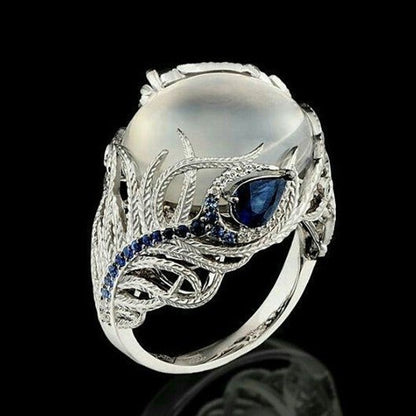 Silver-tone ring with oval white stone, blue center gem, and feather pattern band