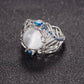 Silver-tone ring with oval white cabochon and blue gemstone accents on carved band
