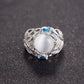 Silver-tone ring featuring oval white stone with blue side gems and ornate feather work