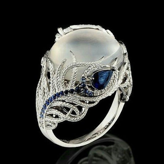 Silver-tone ring with oval white stone, blue center gem, and feather pattern band