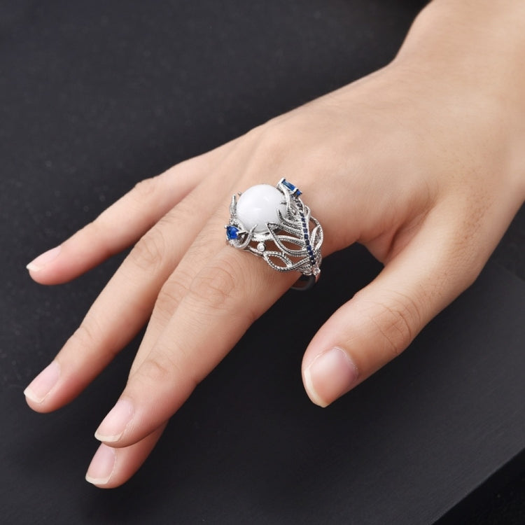 Feather-pattern silver-tone ring with oval white stone and blue gems on a hand