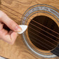 Guitar pick, white triangular pick being used across guitar strings