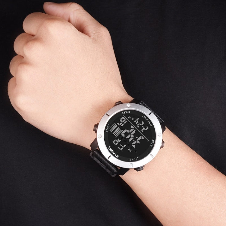 Digital sports watch on wrist with black strap, silver bezel, and teal digital display