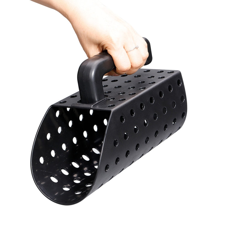 Black perforated sand scoop with long handle, grasped in a hand for digging