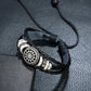 Braided black leather bracelet with circular flower emblem and stacked silver rings