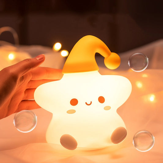 Yellow and white star-shaped silicone bedside night light glowing with hand nearby
