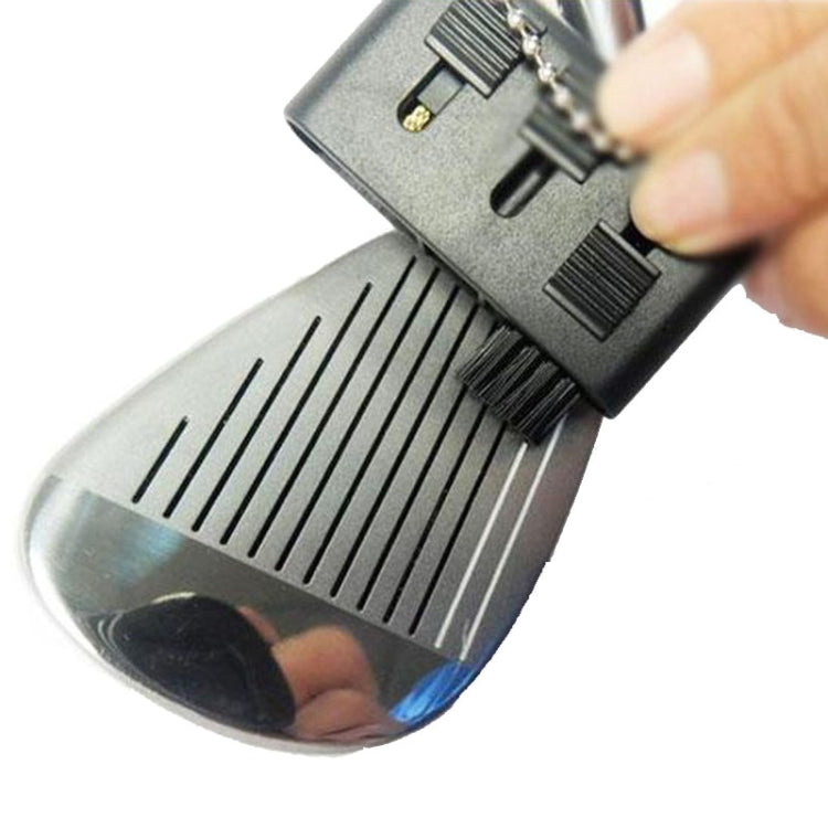 Hand using retractable brush to clean golf iron grooves and ridges