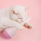 Cat batting a feather tumbler toy with white feathers and purple-and-pink base