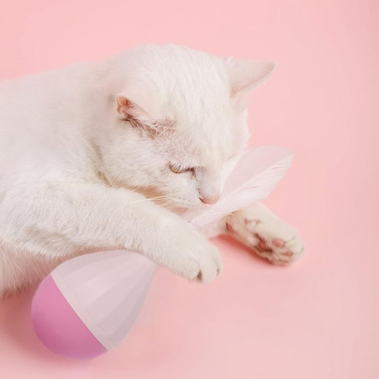Cat batting a feather tumbler toy with white feathers and purple-and-pink base