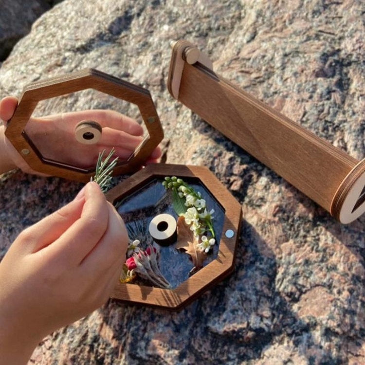 Wooden rotating kaleidoscope toy with octagon window, held near rocky surface