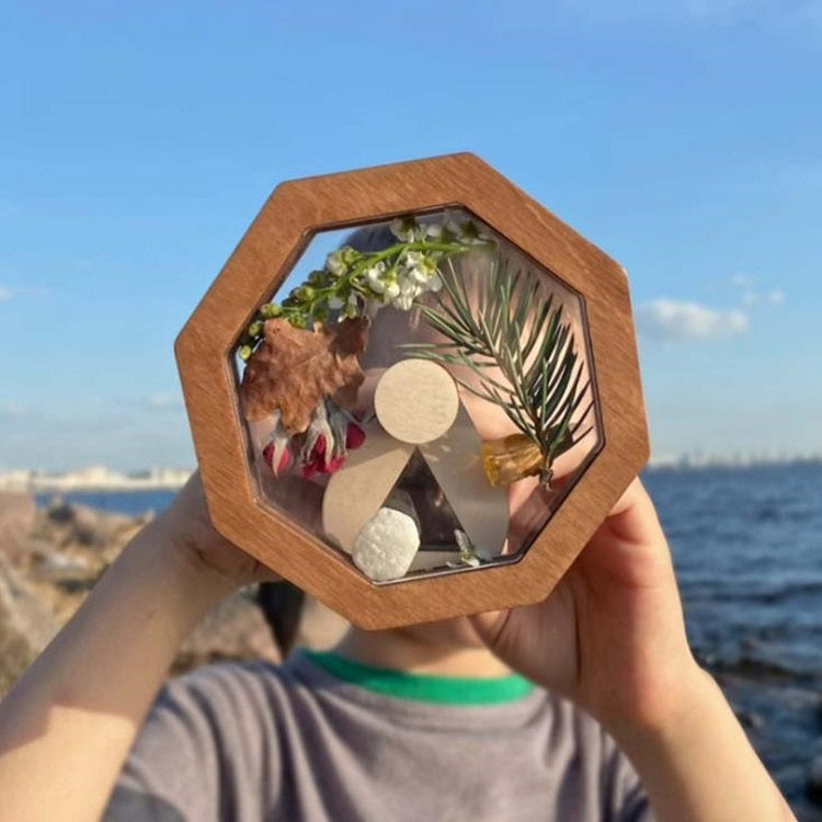 Wooden kaleidoscope toy with octagon viewing window held up by two hands by sea