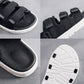 Black slip-on sneakers with textured upper, hook-and-loop strap, and cushioned sole