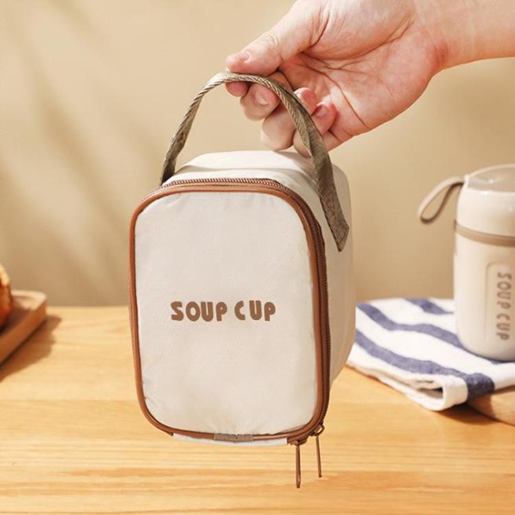 Insulated thermal tote bag held by the gray handle, cream body, “SOUP CUP” text