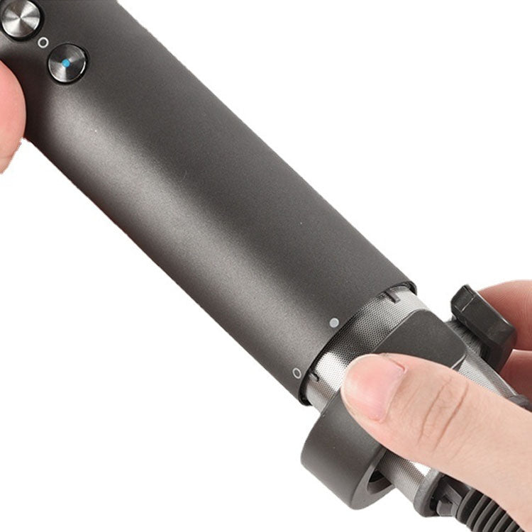 Hand holding a gray cylindrical cleaning brush attachment on a hair tool