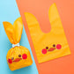 Rabbit-ear gift bag, yellow with red nose and winking cartoon bunny face.