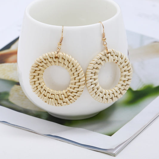 Handmade woven circular hoop earrings on gold-tone ear hooks, natural beige fiber.