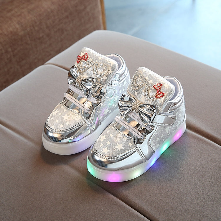 Kids flashing sneakers, metallic silver stars and red bow, angled front with multicolor LED sole