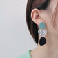 Long dangle earrings worn: teal circles with leaf-print and black oval drops