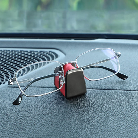 Car dashboard eyeglass holder with black case securing red wire-framed glasses
