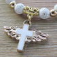 Angel cross charm on white beads with gold spacer beads, close-up.