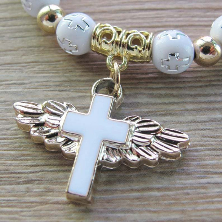 Angel cross charm on white beads with gold spacer beads, close-up.