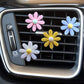 Multiple daisy air vent aromatherapy clips in pink, blue, yellow, and white on car vent