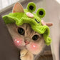 Green knitted frog hat on cat, with black eye openings and small pink nose